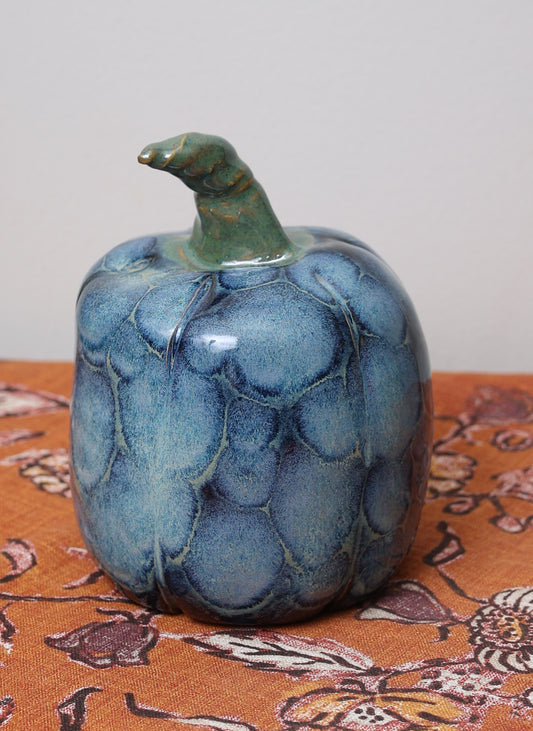 Icy blue glazed ceramic pumpkin with upright green stem.