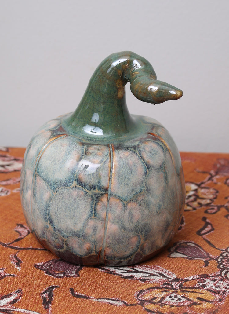Neutral ceramic pumpkin with textured glaze and long curled green stem.